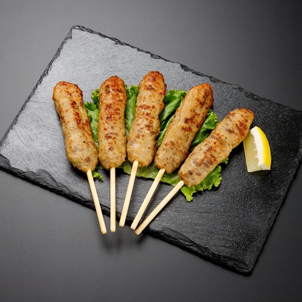 石板に並べた串刺しの牛たんつくね5本と、添えられたレモン