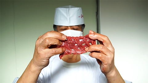 白衣とマスク姿の職人が、キッパを入れた牛たん一枚を両手で広げて見せている