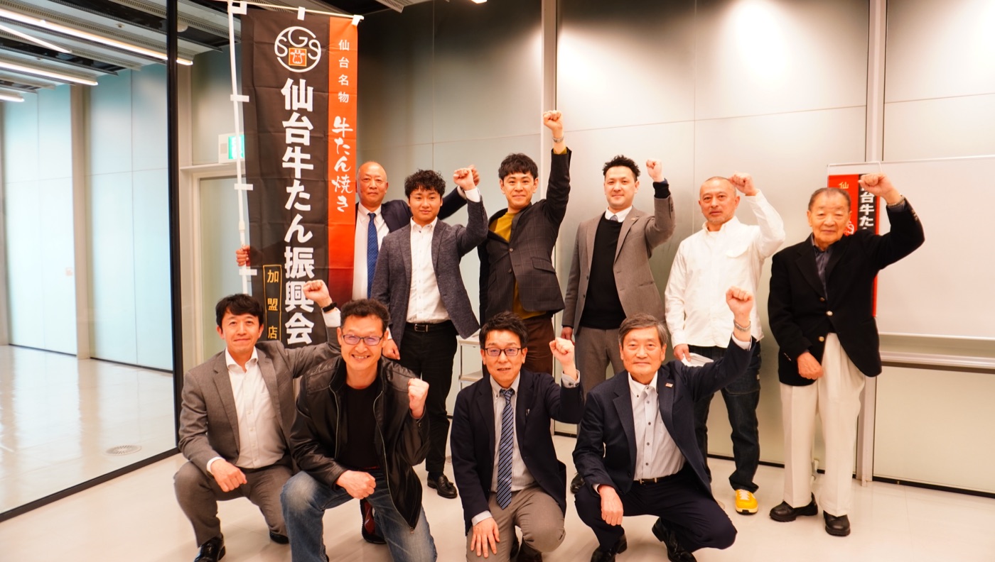 仙台牛たん振興会ののぼりを囲み、こぶしを上げる加盟店メンバーの集合写真（2024年）