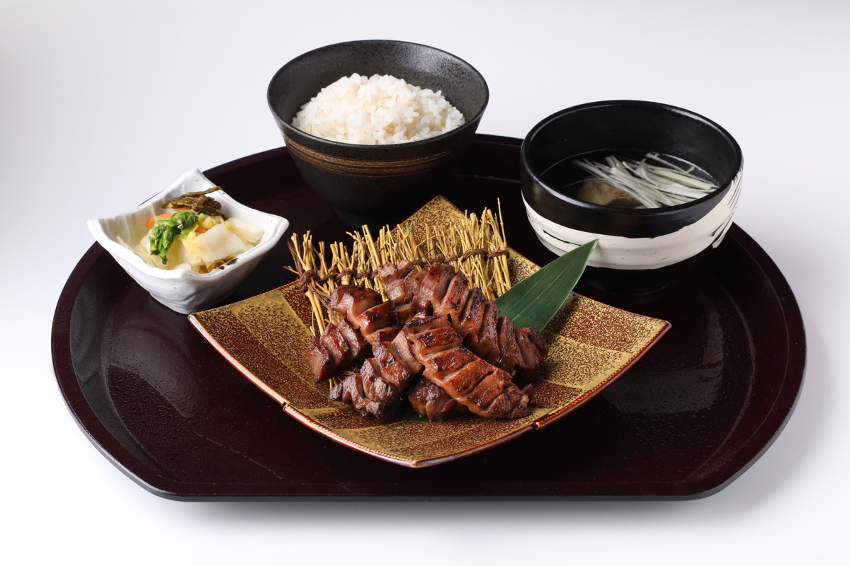 喜助プレミアム極厚弐拾定食（６切 6,050円・2026年8月時点のエスパル店価格）。厚切りの牛たん焼きを金彩の角皿に盛り、麦飯とテールスープ、小鉢を塗りの膳に並べている