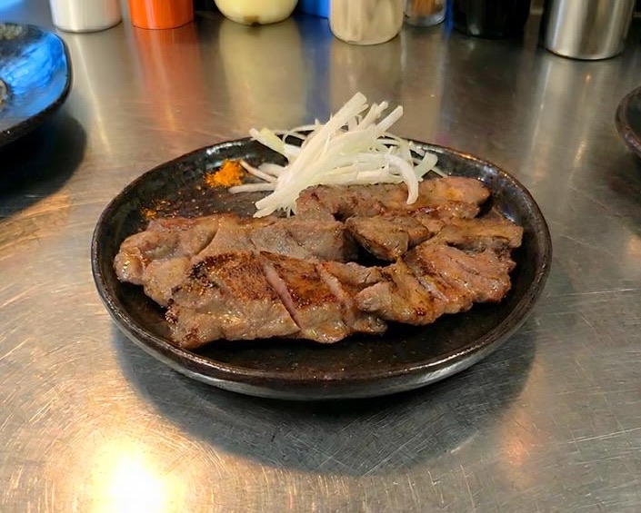 黒い皿に盛り付けた焼き上がりの牛たんと、添えられた白髪ねぎ
